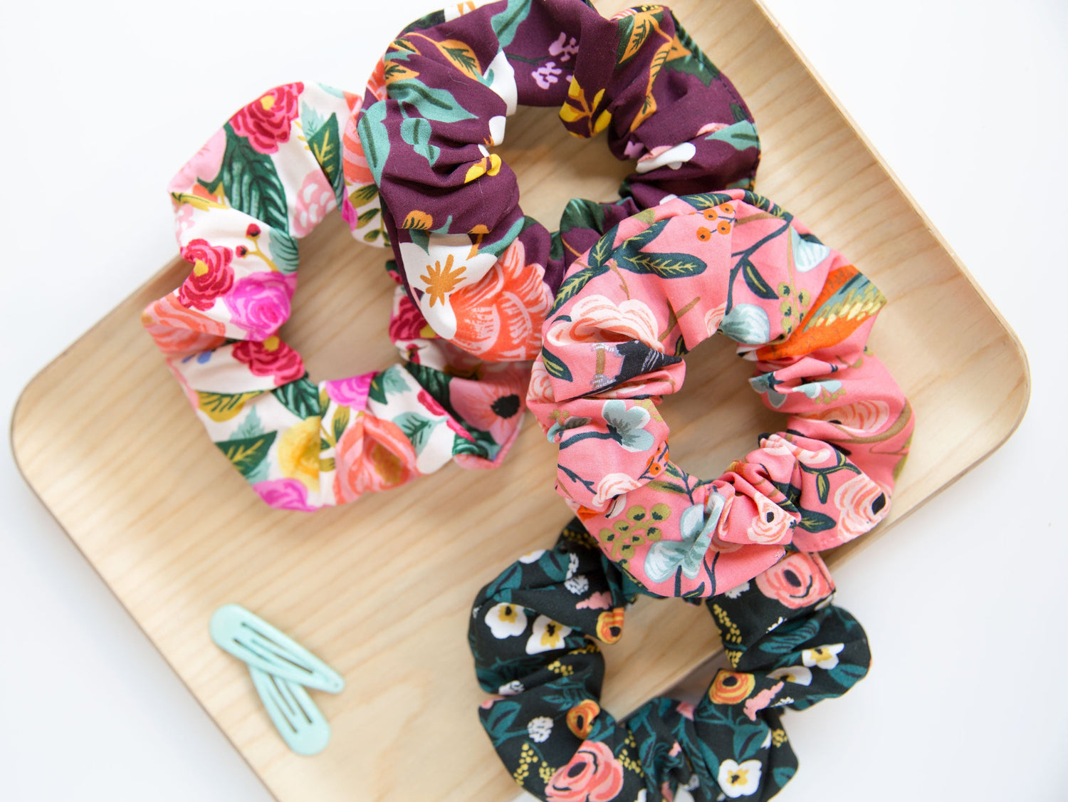 Four floral scrunchies laying on a wooden plate with blue hair clips