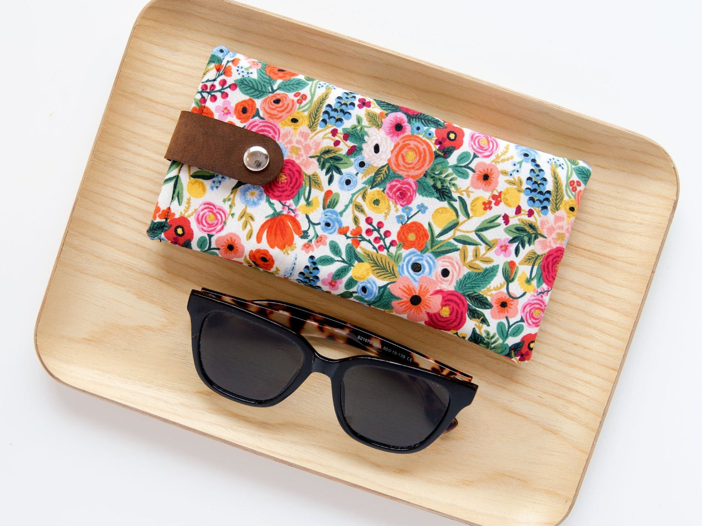 Sunglasses sitting on a wooden plate beside a floral glasses case