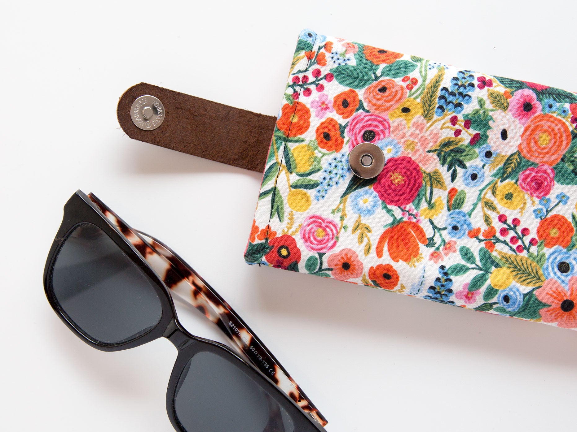 Sunglasses beside a floral glasses case with a magnetic snap